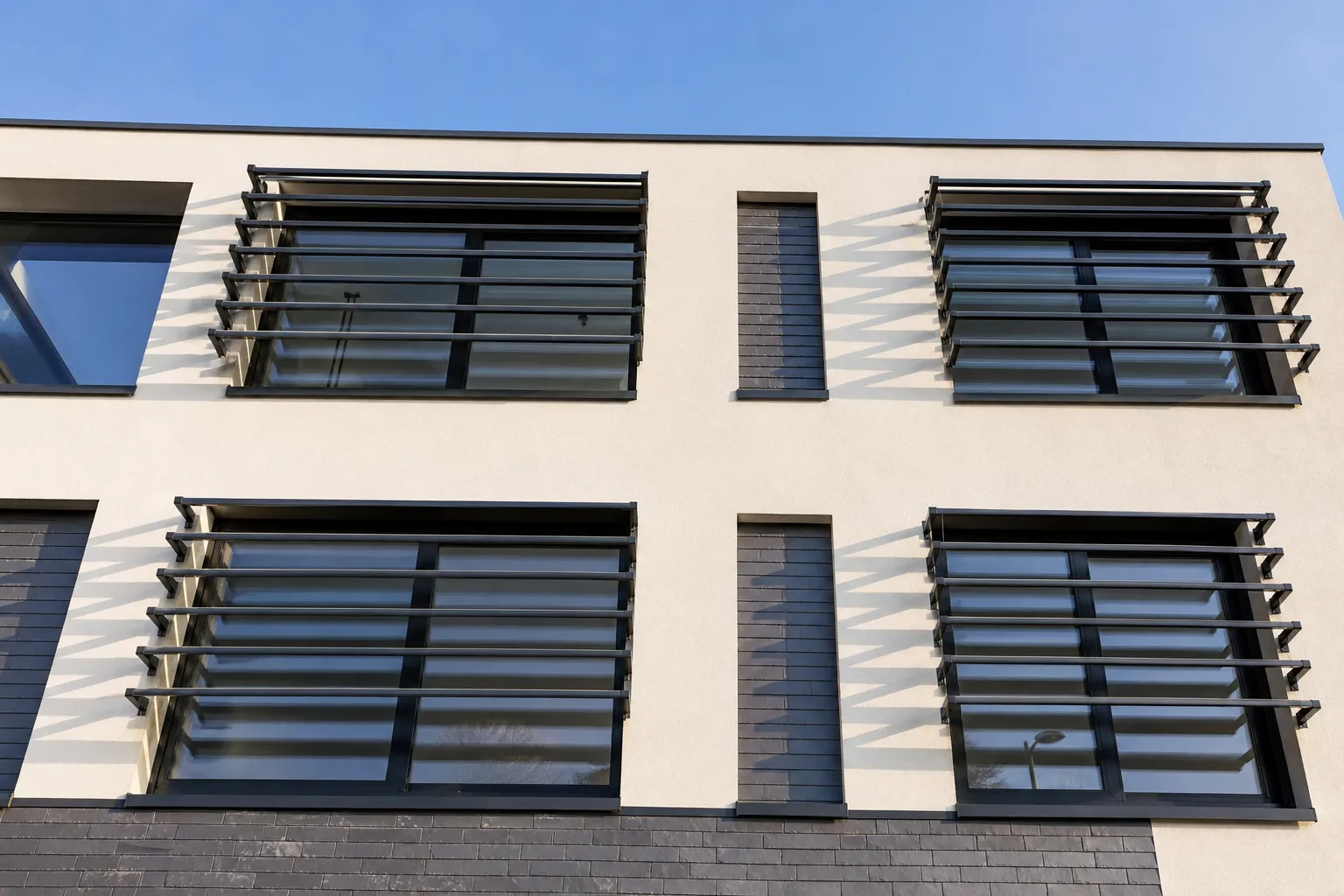 Brise-soleil à lames orientables en aluminium fixé devant une façade, bandes d’ombre projetées