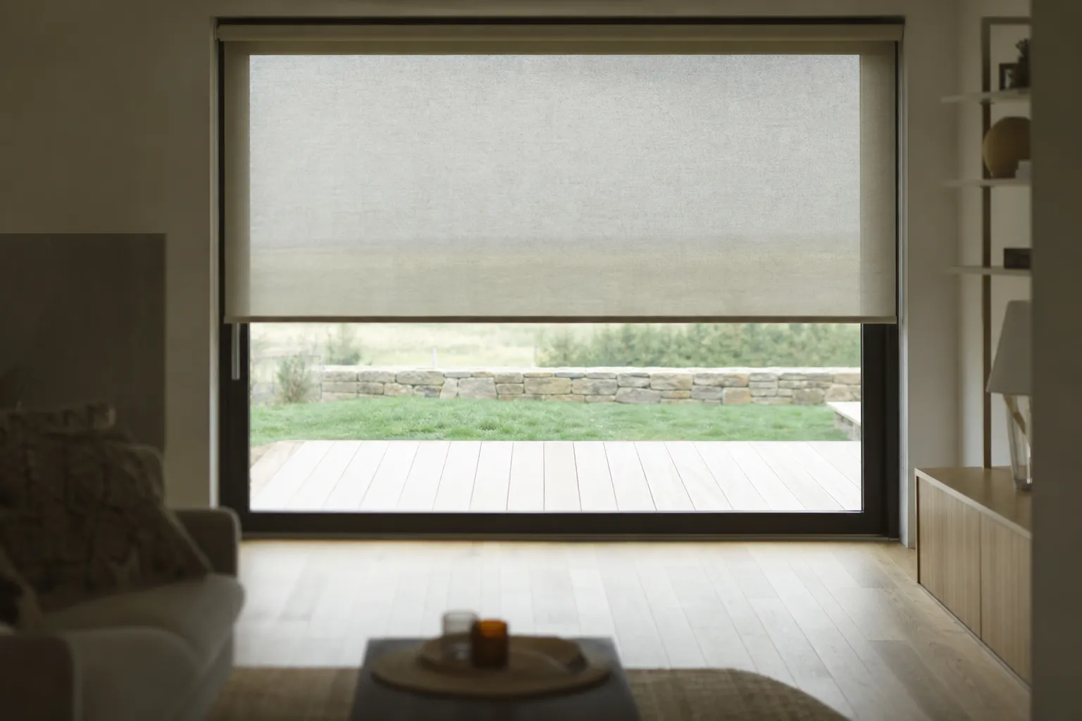 Store intérieur textile descendu à mi-hauteur devant une baie vitrée, lumière filtrée